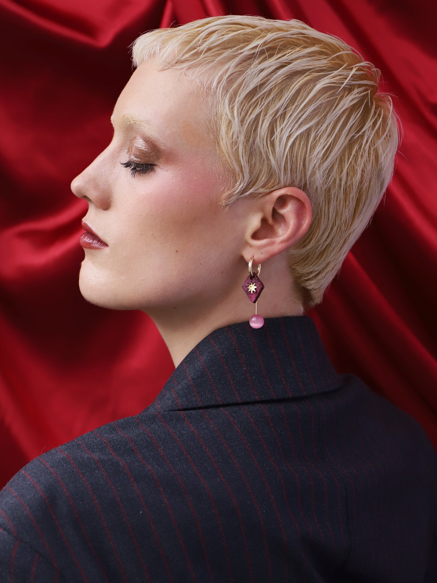 Model showcasing Stella Charm Hoops in Cherry against a rich red backdrop, emphasizing the intricate handmade design.