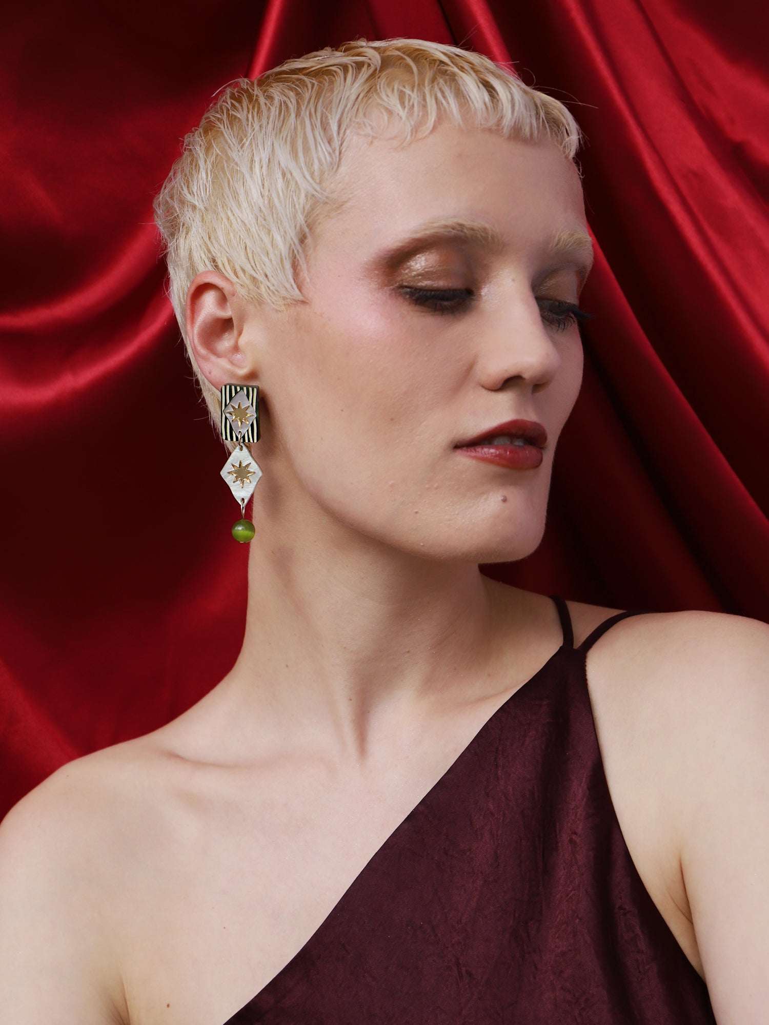 Model wearing Allegra Earrings in Jade with intricate designs, set against a luxurious red backdrop.