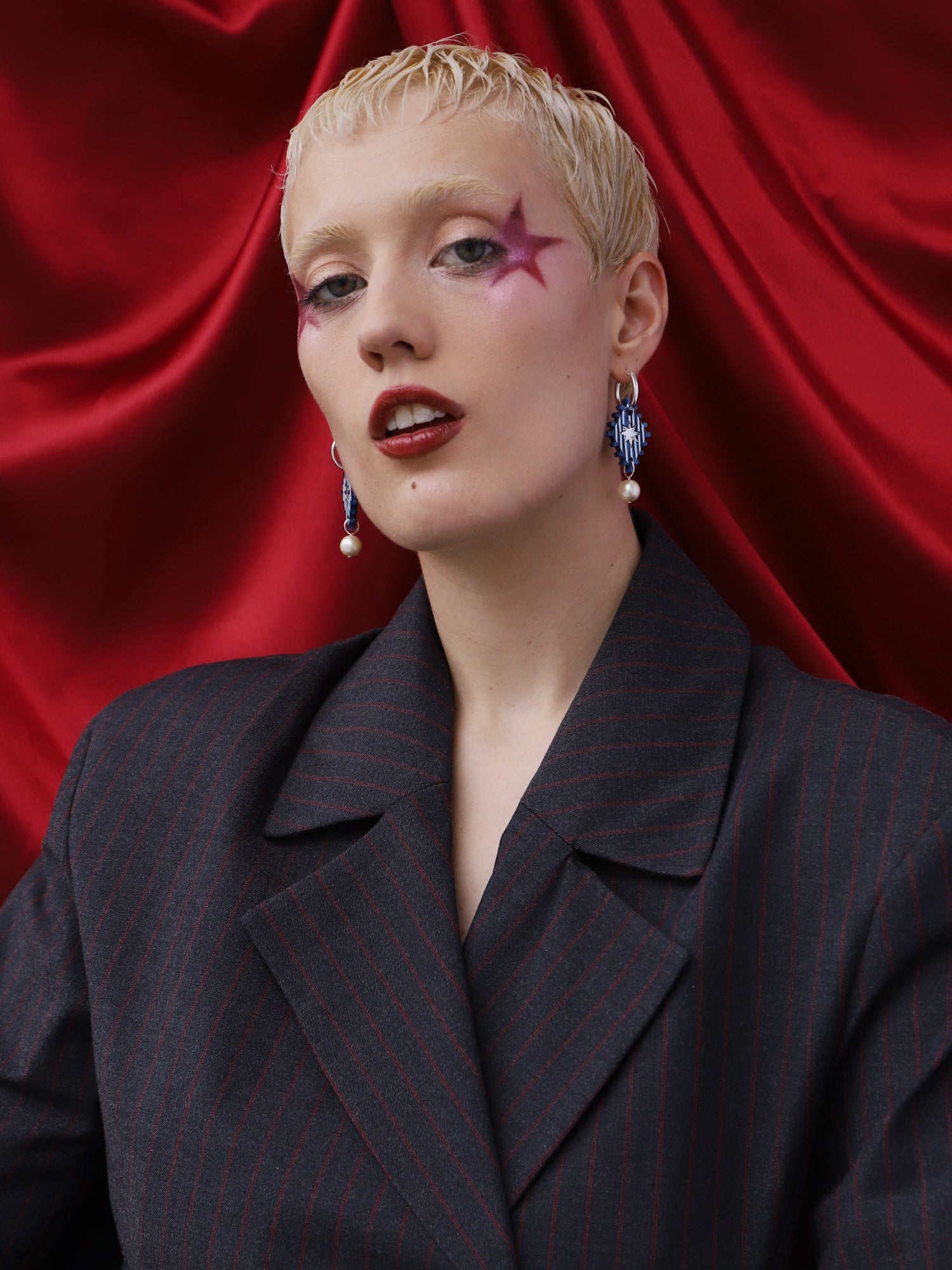 Model wearing Cirque Hoops in Sapphire earrings, featuring hand-inked design, on red background. Handmade in UK by Wolf & Moon.