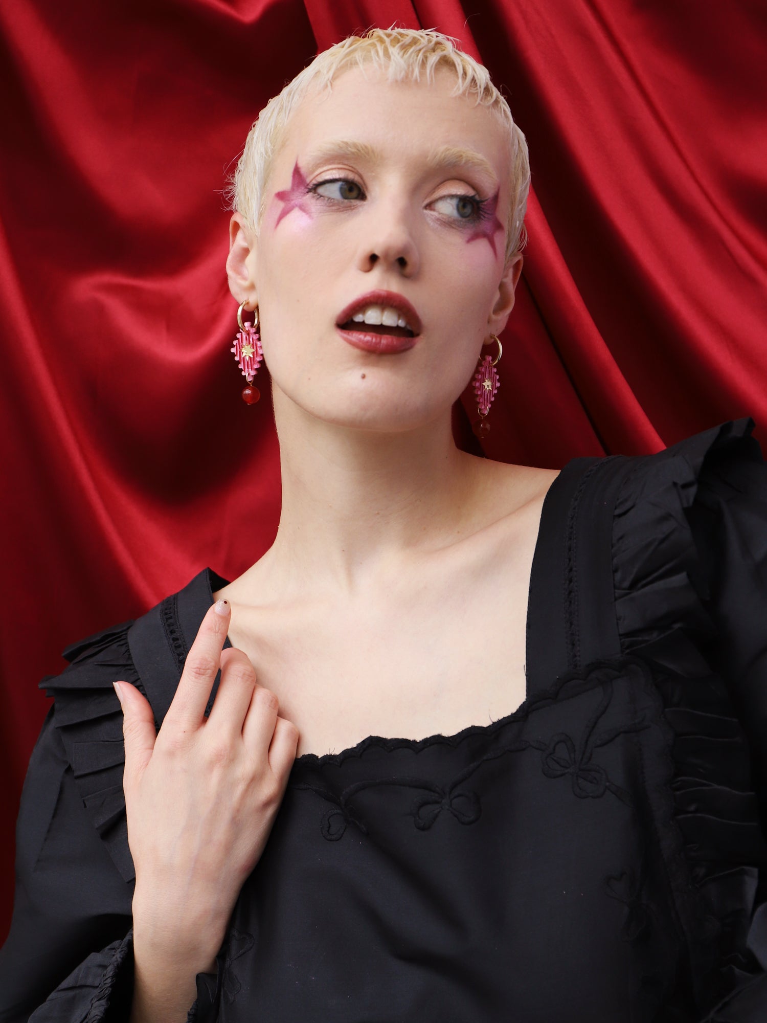 Model wearing Cirque Hoops in Rose earrings, handmade in UK by Wolf & Moon, against red background.
