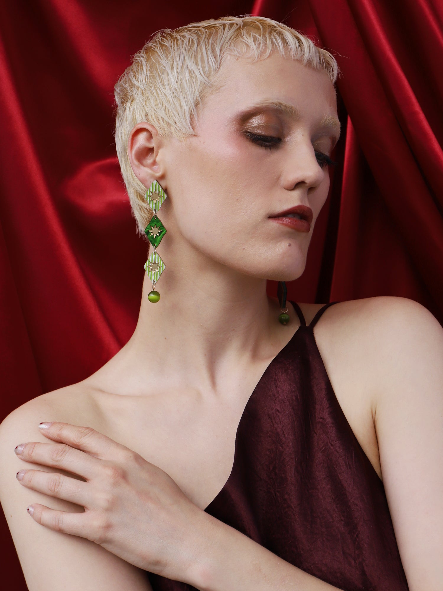 Harley Statement Earrings in Jade worn by a model against a red backdrop, showcasing their unique design and color.