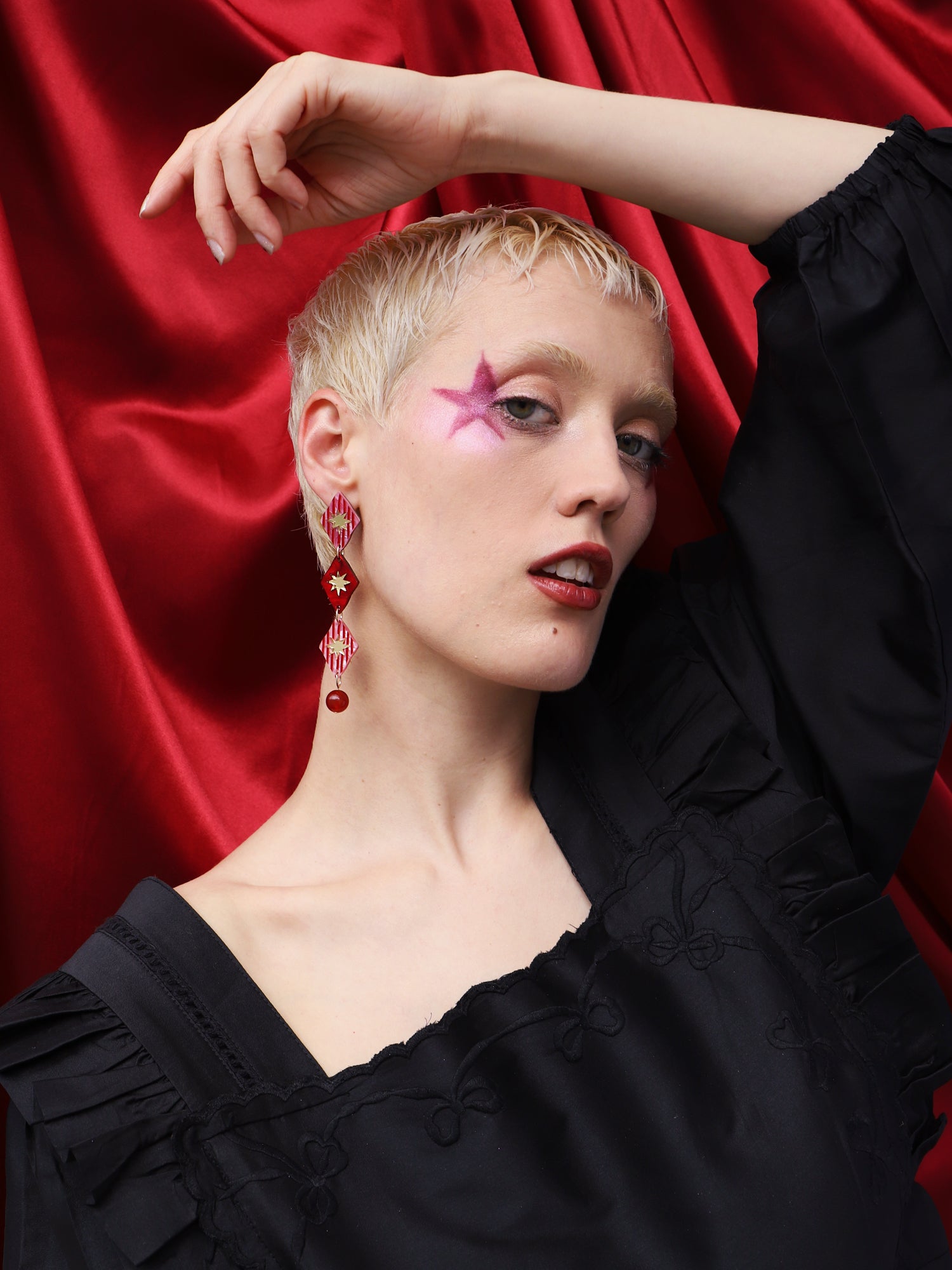 Model showcasing Harley Statement Earrings in Rose against a red backdrop, highlighting intricate design and vibrant colors.