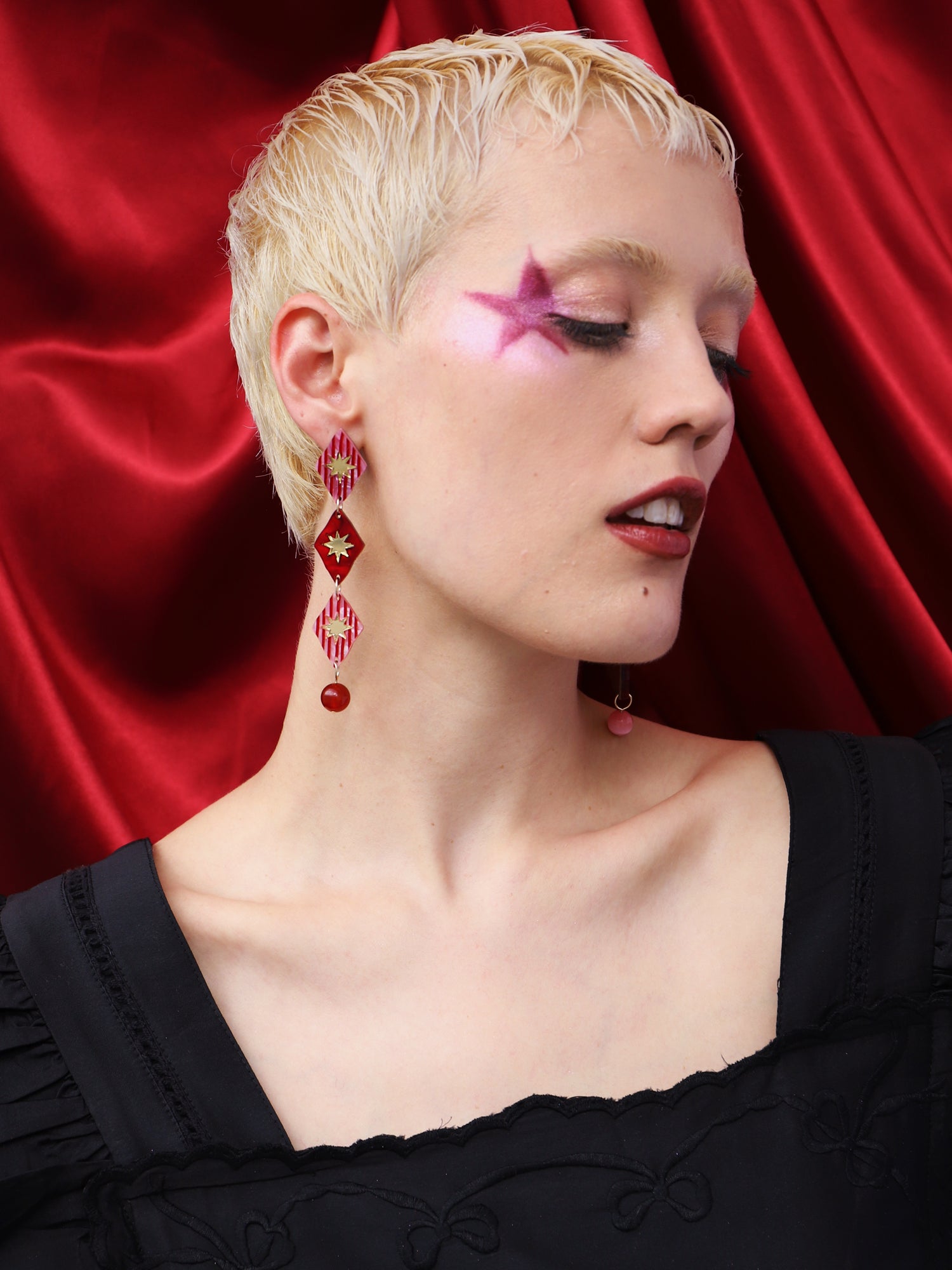 Model wearing Harley Statement Earrings in Rose against a red backdrop, showcasing the intricate design and vibrant colors.