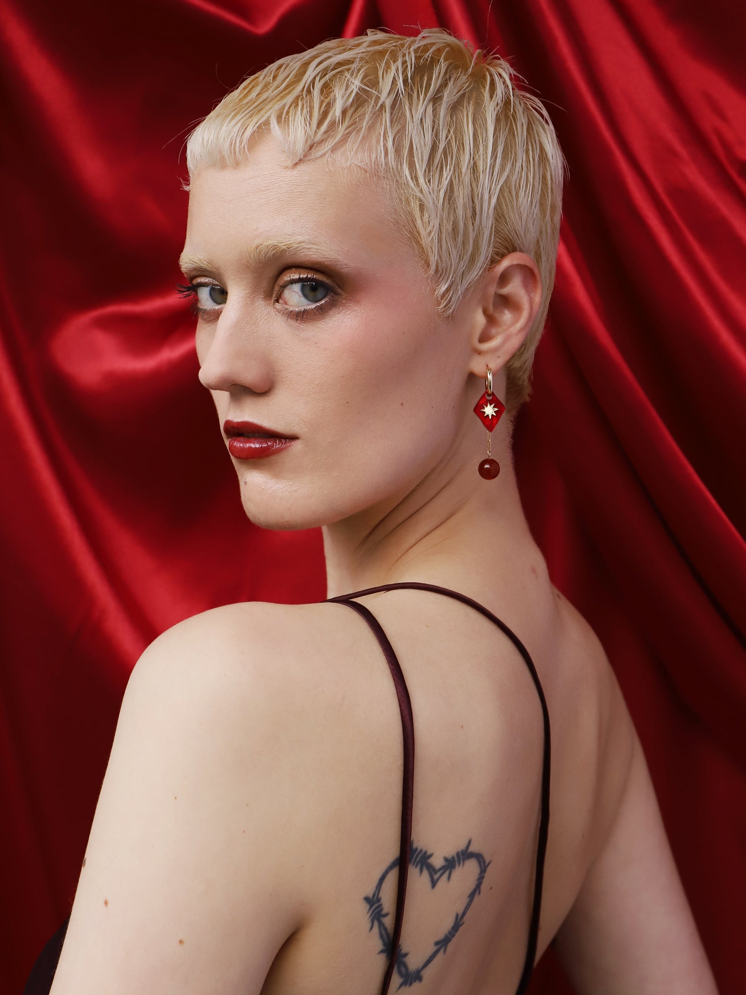 Kaleido Charm Hoops Set in Rose worn by model against a red backdrop, showcasing unique charms and handmade design by Wolf & Moon.