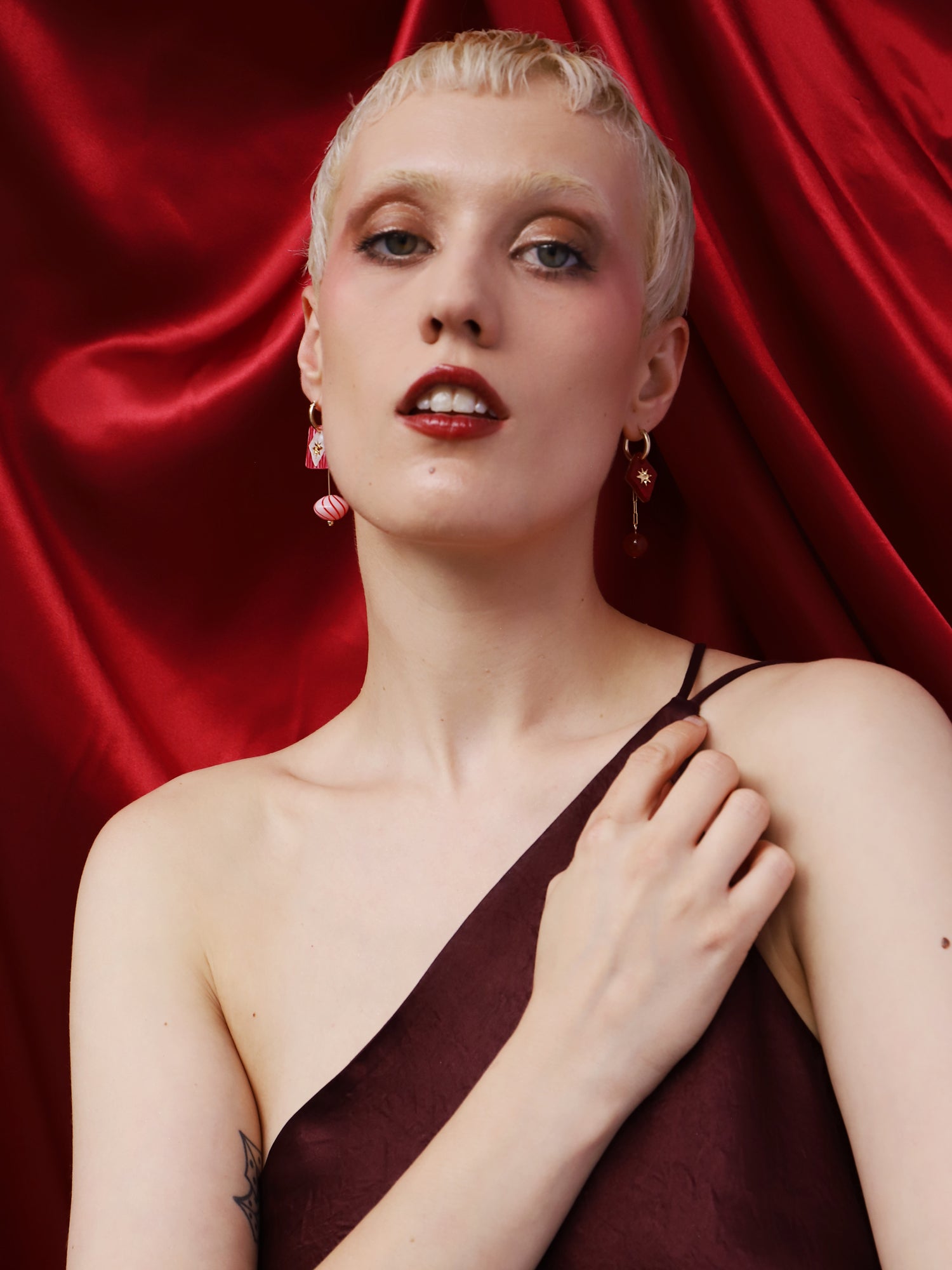 Model wearing Kaleido Charm Hoops Set in Rose against a red satin background, showcasing handmade details by Wolf & Moon.