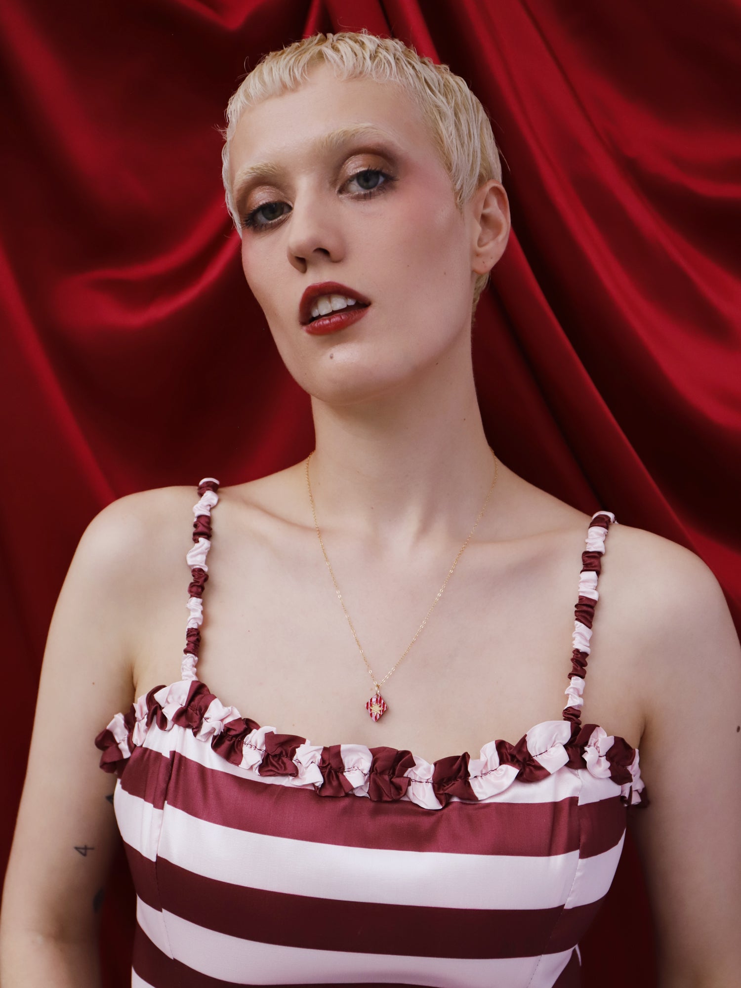Nova Necklace in Rose worn by model with short blonde hair, featuring a red and white striped dress, against a red backdrop.