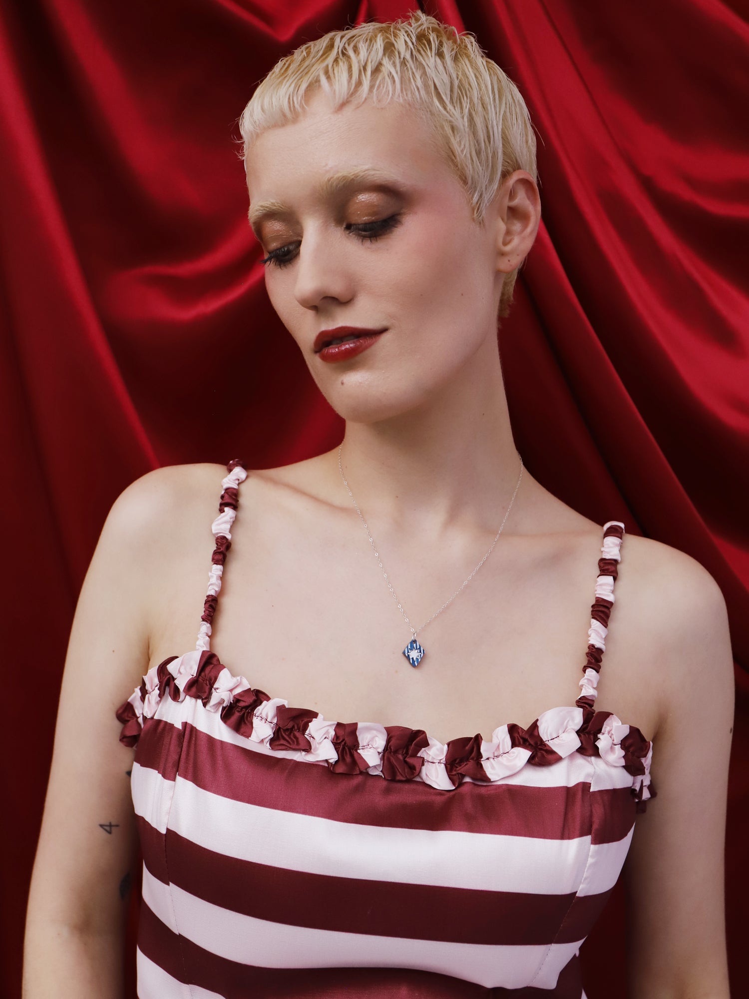 Model wearing the Nova Necklace in Sapphire, handmade in UK by Wolf & Moon, against a red backdrop.