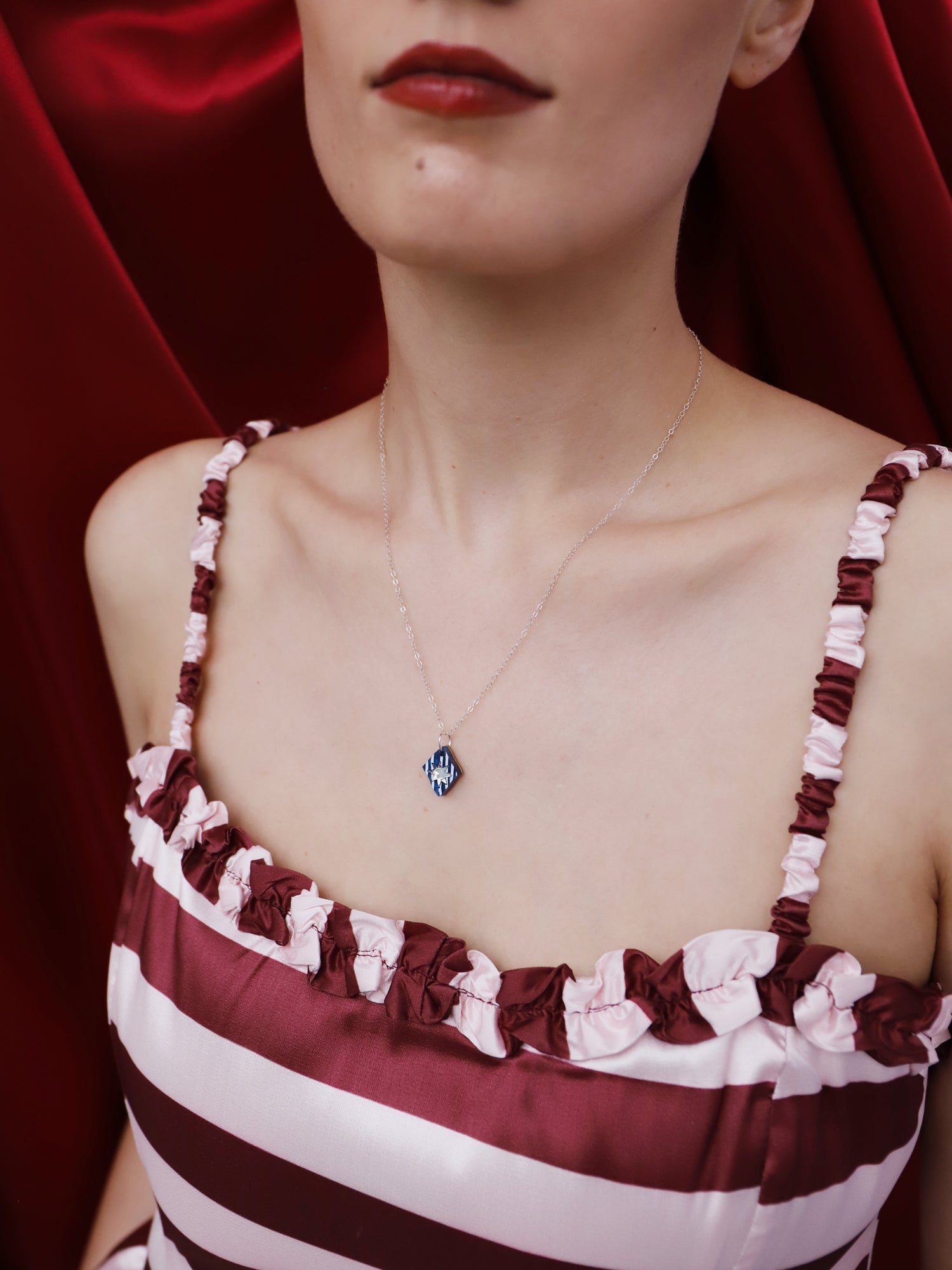 Model wearing Nova Necklace in Sapphire with a maroon and white striped dress, showcasing its unique design.