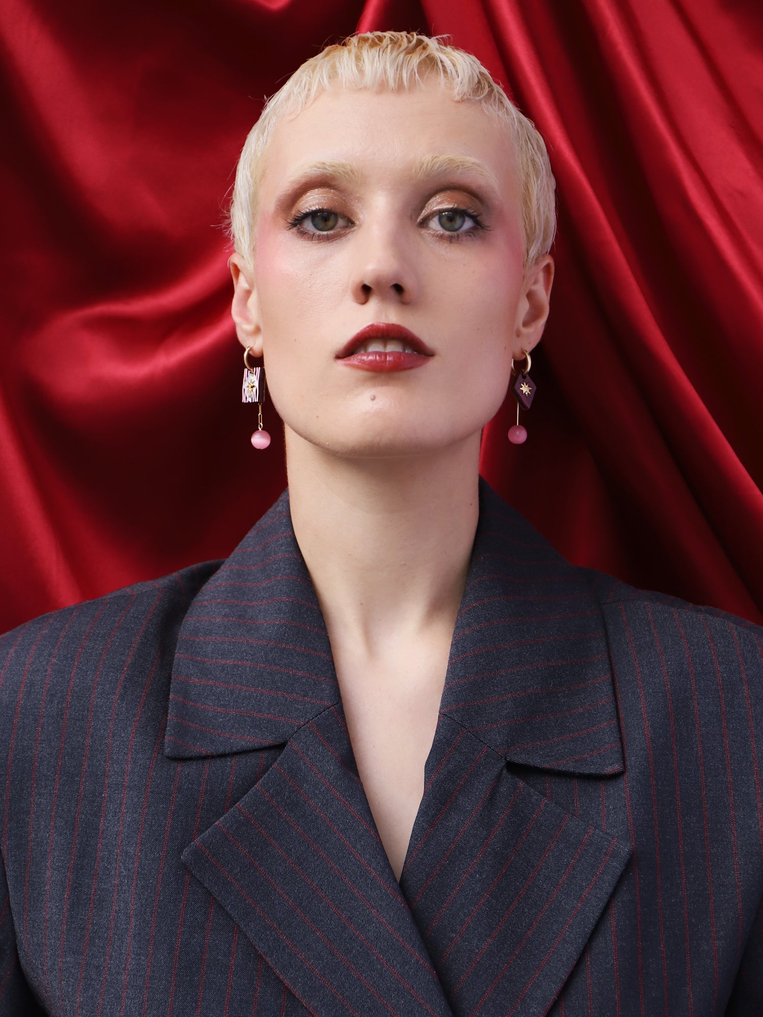 Stella Charm Hoops in Cherry showcased on model against a red backdrop, featuring unique charms and intricate design.