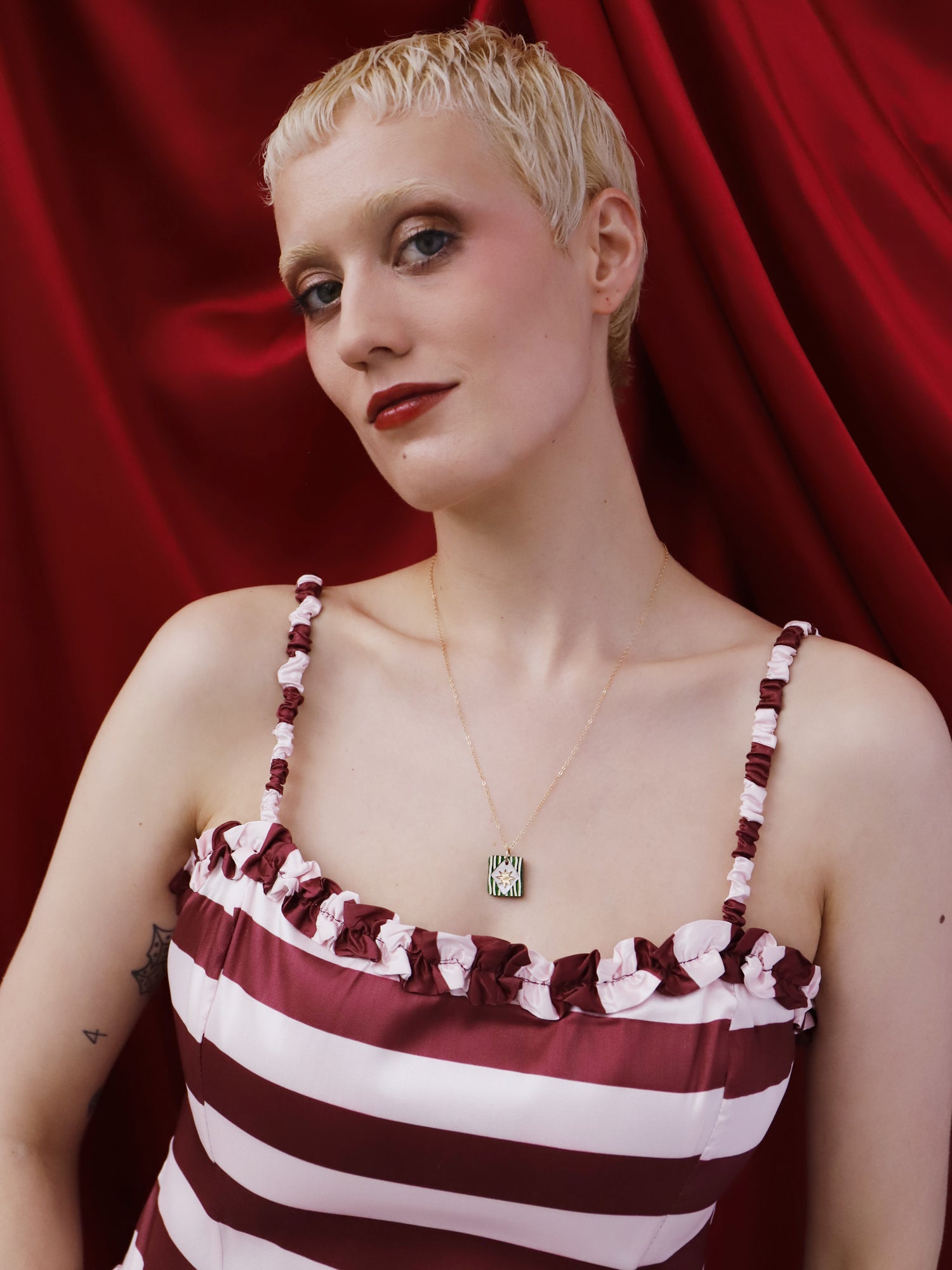 Model wearing Stella Necklace in Jade on a gold-filled chain, featuring hand-inked details, against a red backdrop.