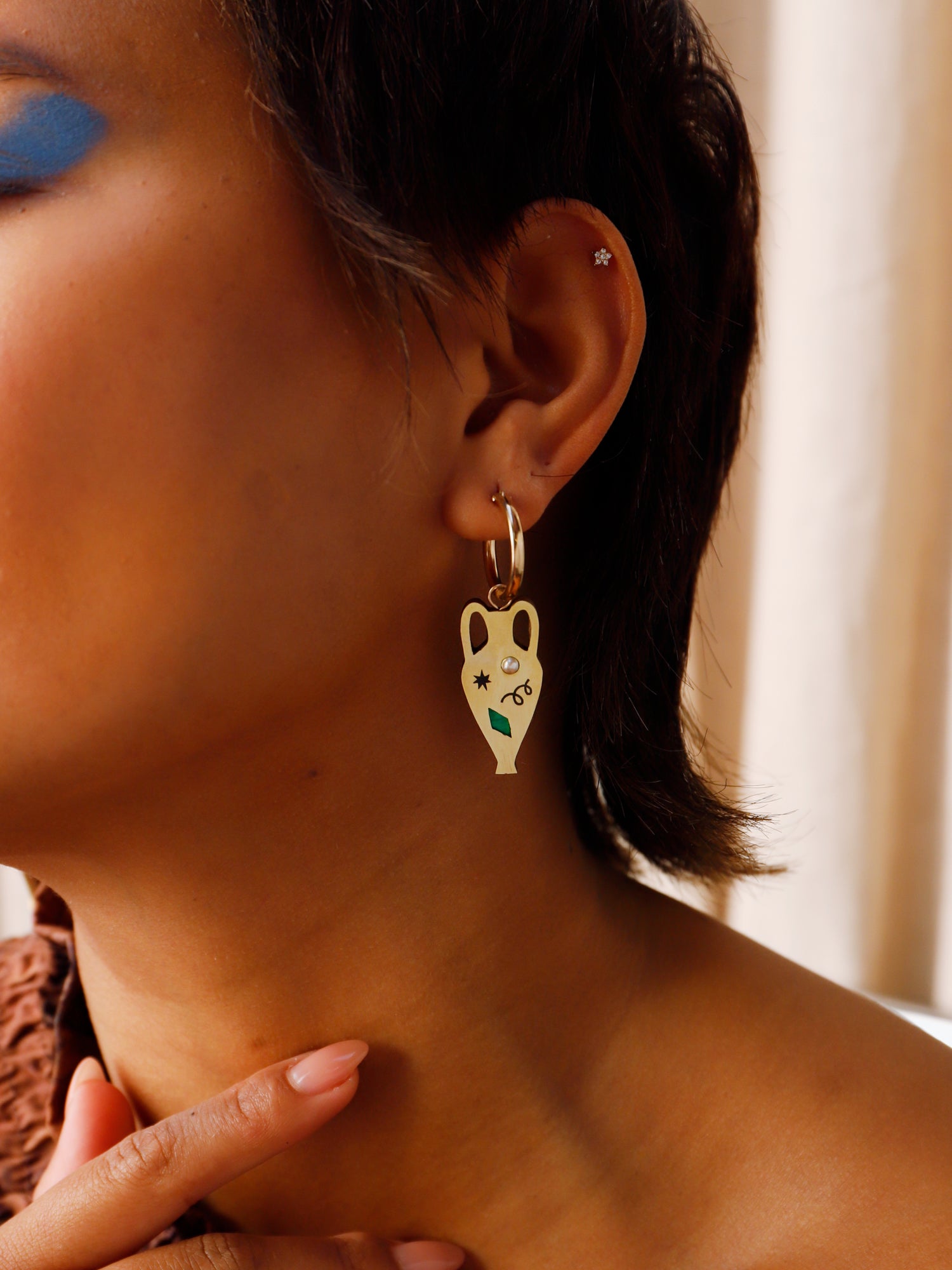 Brass vase shape hoop earrings. Glass pearls and abstract cut outs with inlaid shell and illustrative detailing.