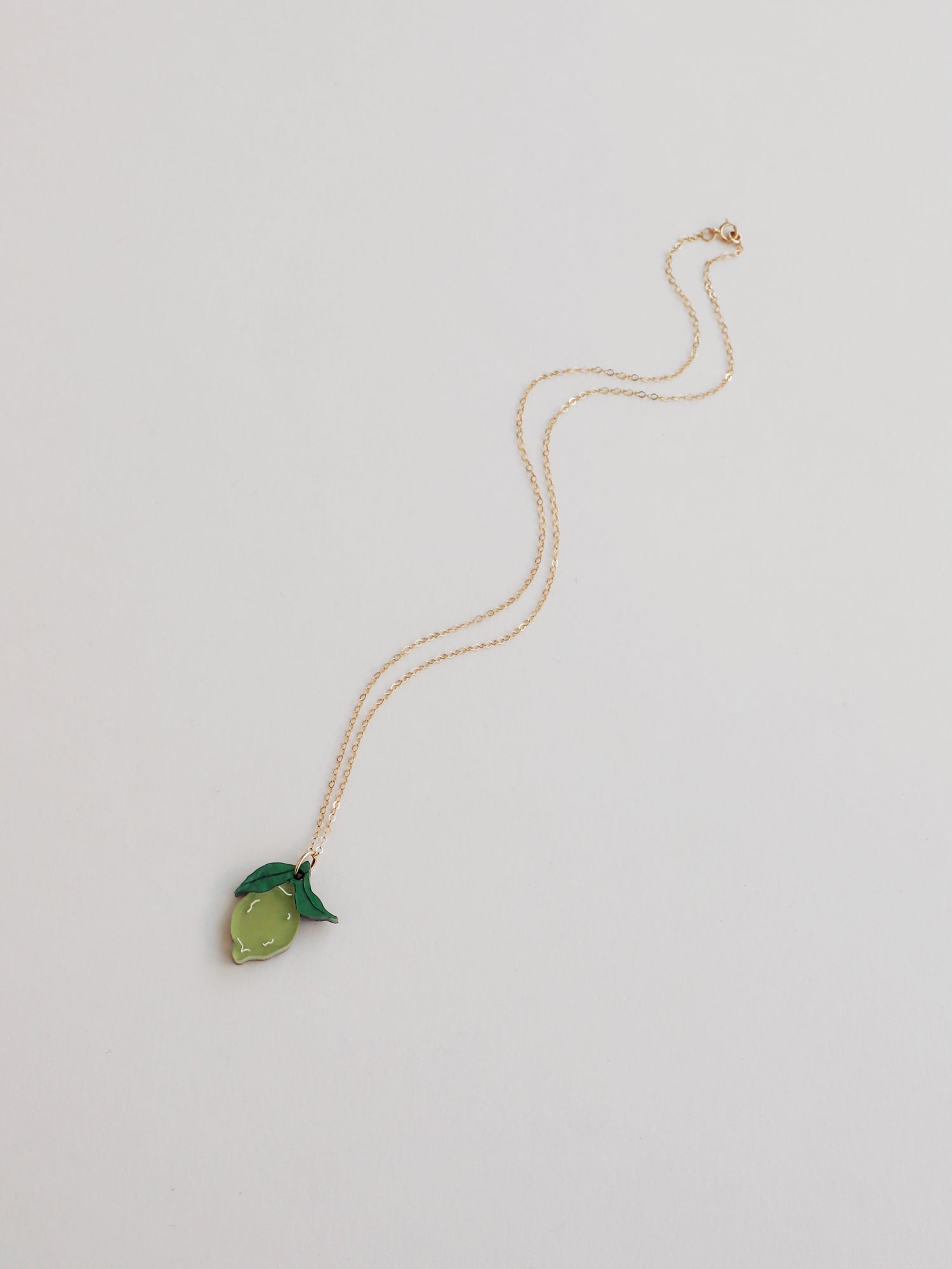 Lime pendant necklace with green leaf made with wood, 64% recycled acrylic and hand-inked details. Hung on a high quality 45cm gold-filled chain. Handmade in the UK by Wolf & Moon.