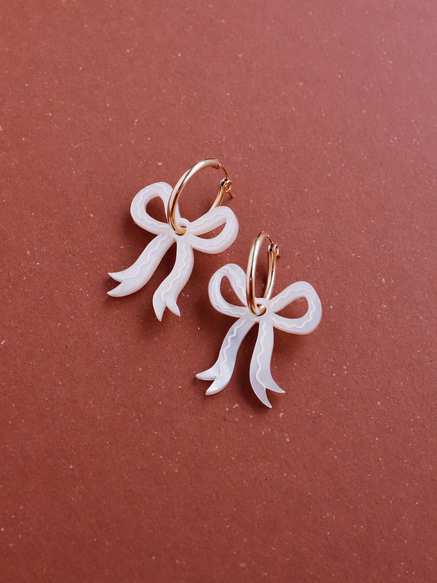 Romantic mini bow earrings in off-white made from velvety marbled acrylic with hand-inked details. Surprisingly lightweight so can be worn for extended periods of time. Each bow is hand-sculpted into a 3D form giving it a lovely realistic ribbon-like effect. This also adds a unique charm to each one. Handmade by Wolf & Moon in the UK. ⁠